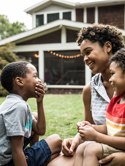 Single mother playing with young sons in front of house