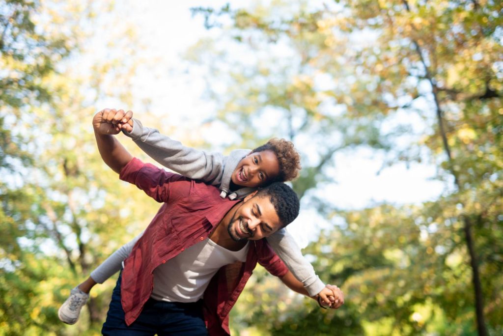 Father carrying daughter piggyback with arms spread